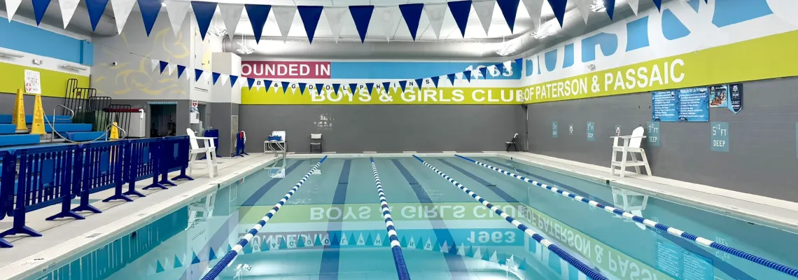 Indoor lap pool inside Boys and Girls Club of Paterson and Passaic, with lifeguard chairs and some bleacher-style seating.