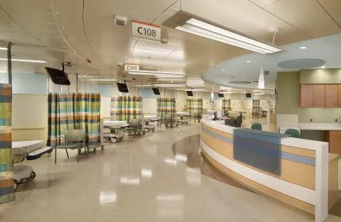 Pre-surgical area of St. Joseph's University Medical Center, with a row of hospital beds separated by privacy curtains, and a staff counter and work area.